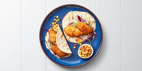 Three soft fish tacos with crumbed fillets, red cabbage slaw, and a side of zesty corn salsa on a blue plate.