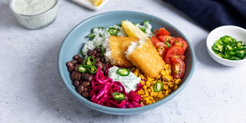 Fish taco bowl with crumbed fish fillets, rice, black beans, corn, cherry tomatoes, pickled cabbage, jalapeños, and creamy dressing.