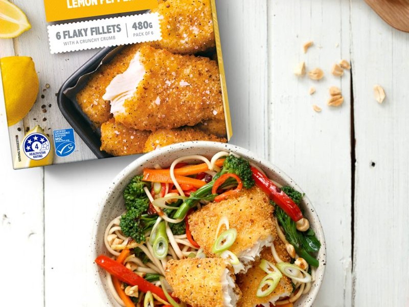 box of sealords frozen lemon pepper hoki fillets placed on wooden bench next to a dish that contains a noodle stir-fry and sealords hoki fish. foodstuffs proposal accepted, Nz