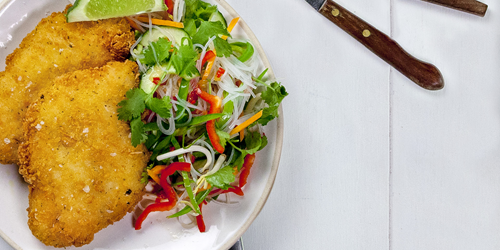 Crispy Thai lime and coconut fish fillets served with a vibrant Asian noodle salad, topped with fresh coriander, red capsicum, and a lime wedge.
