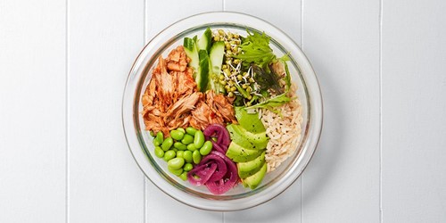 A colourful tuna Buddha bowl with brown rice, flaked tuna, avocado, edamame, pickled onion, cucumber, sprouts, greens, and asparagus, arranged in a glass bowl.
