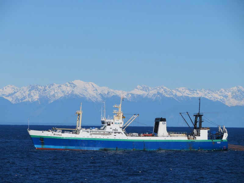 Large commercial fishing vessel at sea with snow-capped mountains in the background under a clear blue sky.