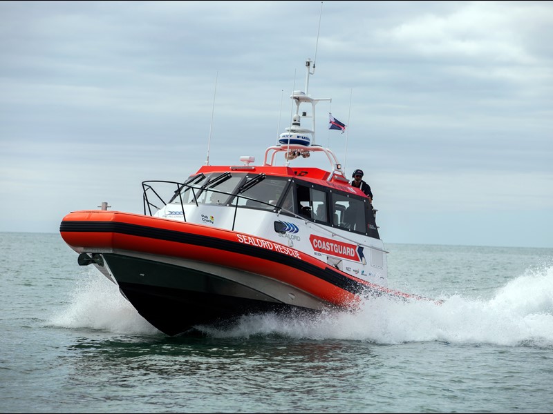 Sealord-branded Coastguard rescue vessel speeding across the water, with a crew member visible and a New Zealand flag flying.