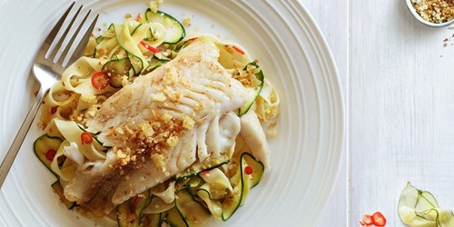 Plate of creamy hoki fillet served over ribbon pasta with sliced courgettes, chilli, and crispy garlic topping.