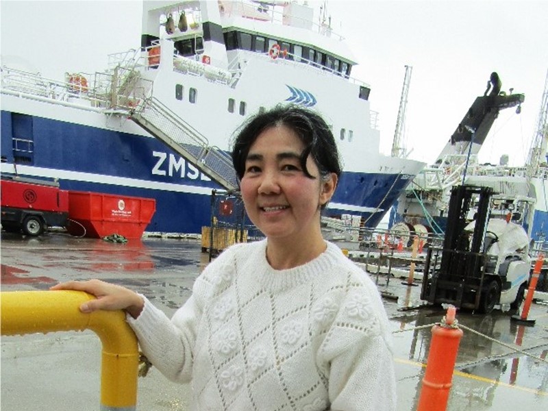 woman in a white knit jersey with dark hair in a pony tail standing in front of a sealords vessel at the doc.