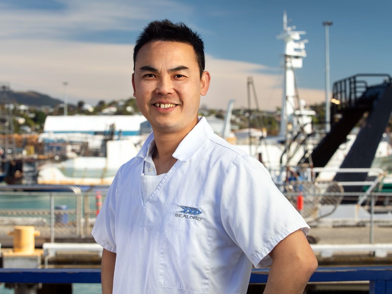 sealord worker wearing the sealord white inform top, posed with their hands on hips in front of the doc