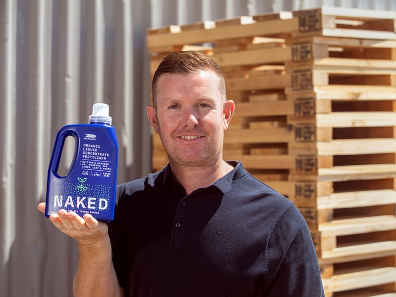 man holding sealord naked fertiliser product infront of a tin shed and wooden pallets