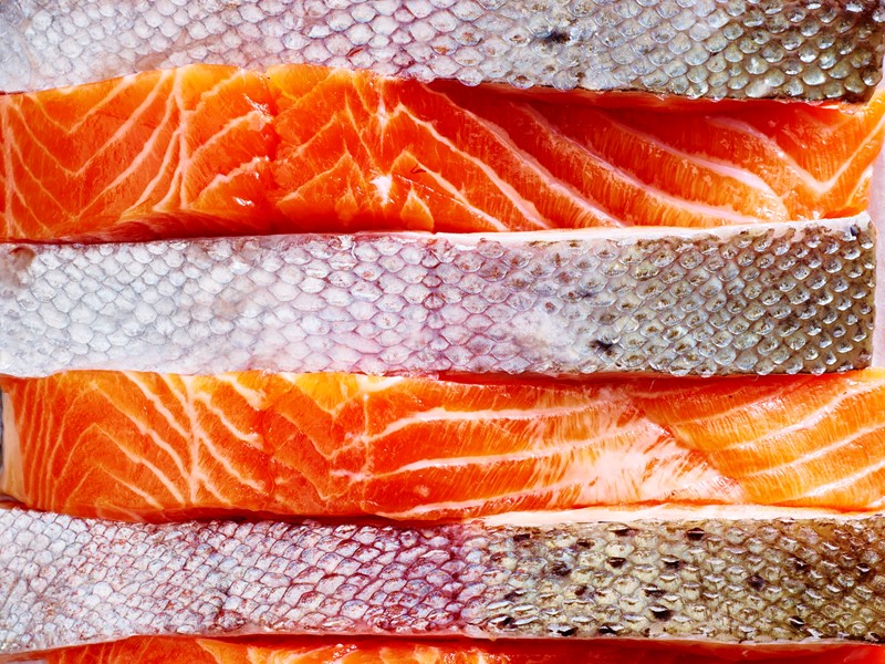 Close-up view of stacked fresh salmon fillets, showing vibrant orange flesh and textured silver skin