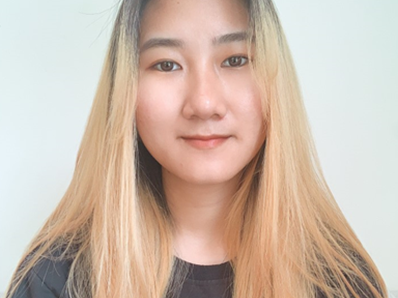 Young woman with blonde hair wearing a black top, taking a selfie against a plain white background.