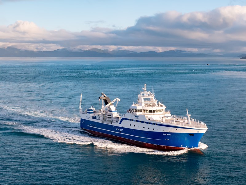 sealord fishing boat is underway in the open ocean, the boat is blue and white, mountains in the distant background