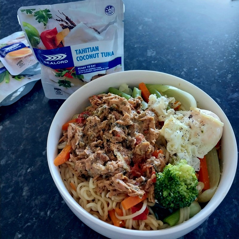 Bowl of cooked noodles topped with Sealord Tahitian Coconut Tuna, mixed vegetables, and a poached egg, with a Sealord tuna pouch in the background