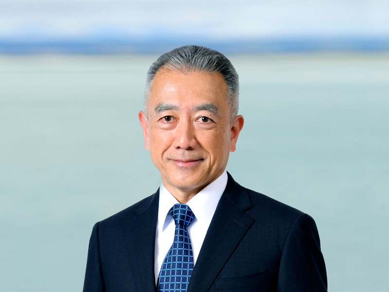 man standing infront of the sea with grey hair and a black and white suit on