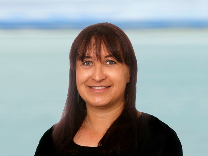 woman standing in front of the sea wth dark hair and a fringe, has a black long sleeve shirt on