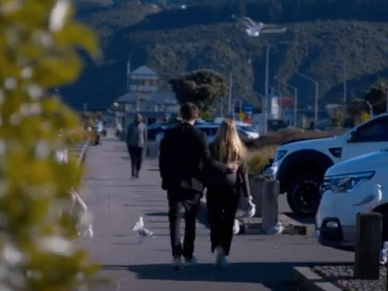 people walking down footpath with cars parked along side during the day.