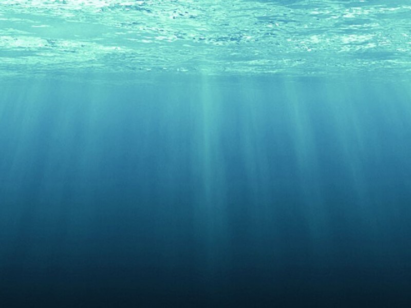 underwater photo of clear blue water with the sun shining through the water to create beams of light.