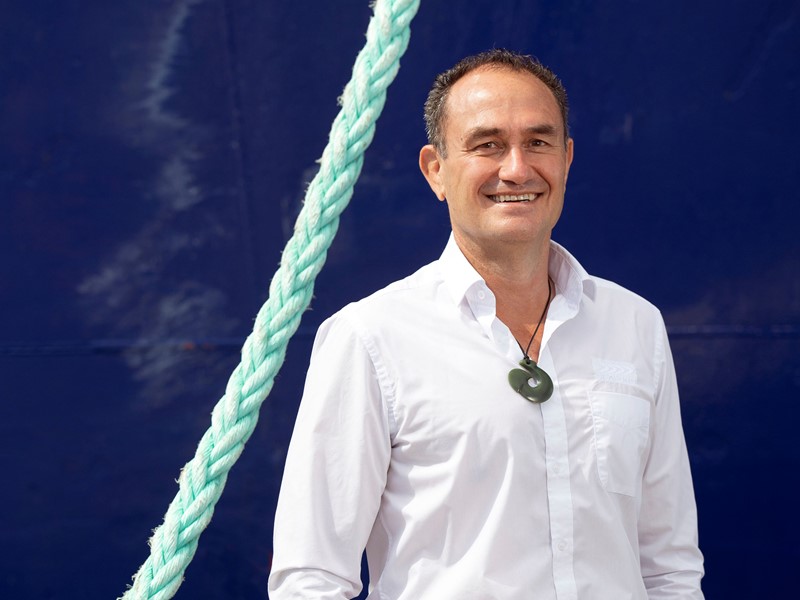 Sealord CEO Doug Paulin in a white shirt standing in front of the bottom of the fishing boat. with a green braided rope hanging beside him