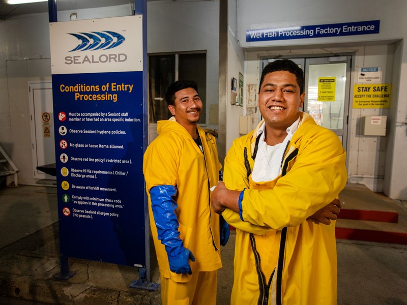 Ricky Smith and Sage Toilalo, from Samoa, standing in a factory wearing yellow overalls, as the first workers to join Sealord’s wetfish factory under the Government’s overseas seafood process worker scheme