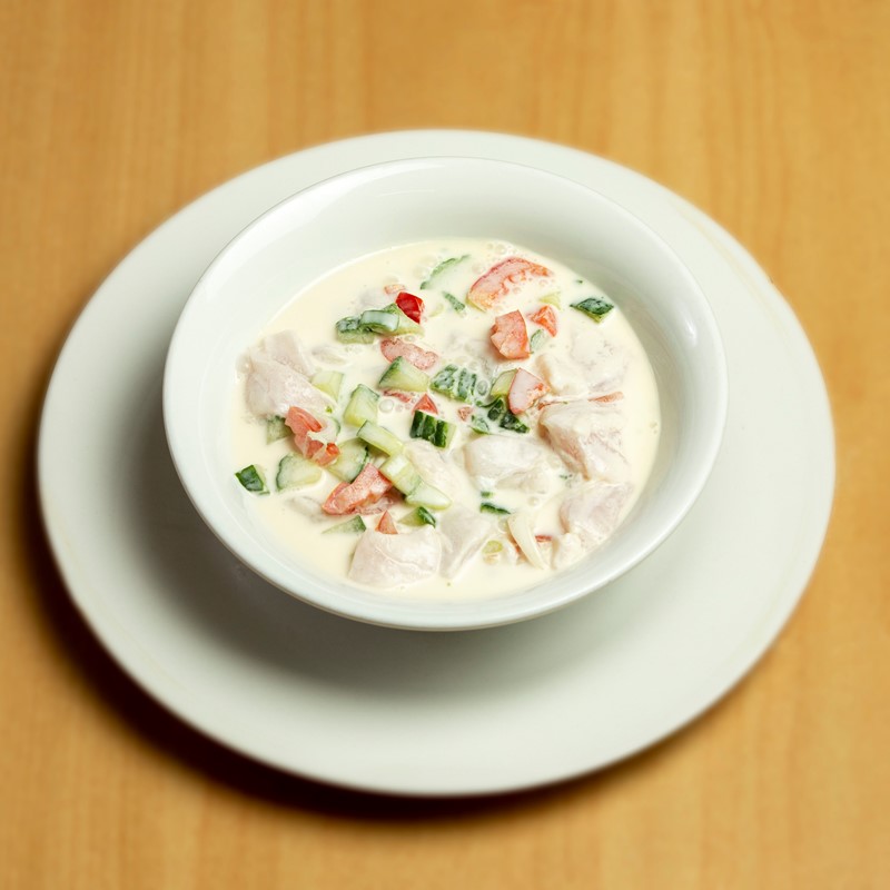 A bowl of coconut fish salad with diced raw fish, cucumber, capsicum, and coconut cream, served on a white plate
