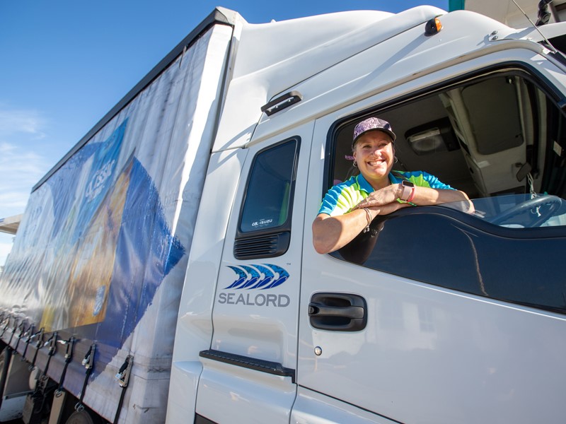 Smiling truck driver leaning out of a Sealord-branded truck window on a sunny day
