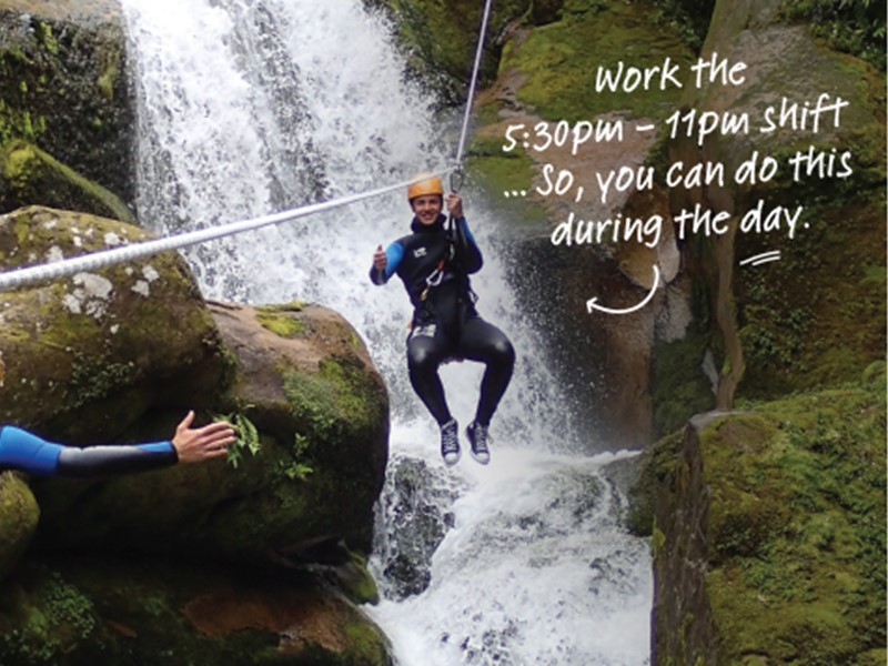 Person ziplining over a waterfall surrounded by mossy rocks, smiling and giving a thumbs up.